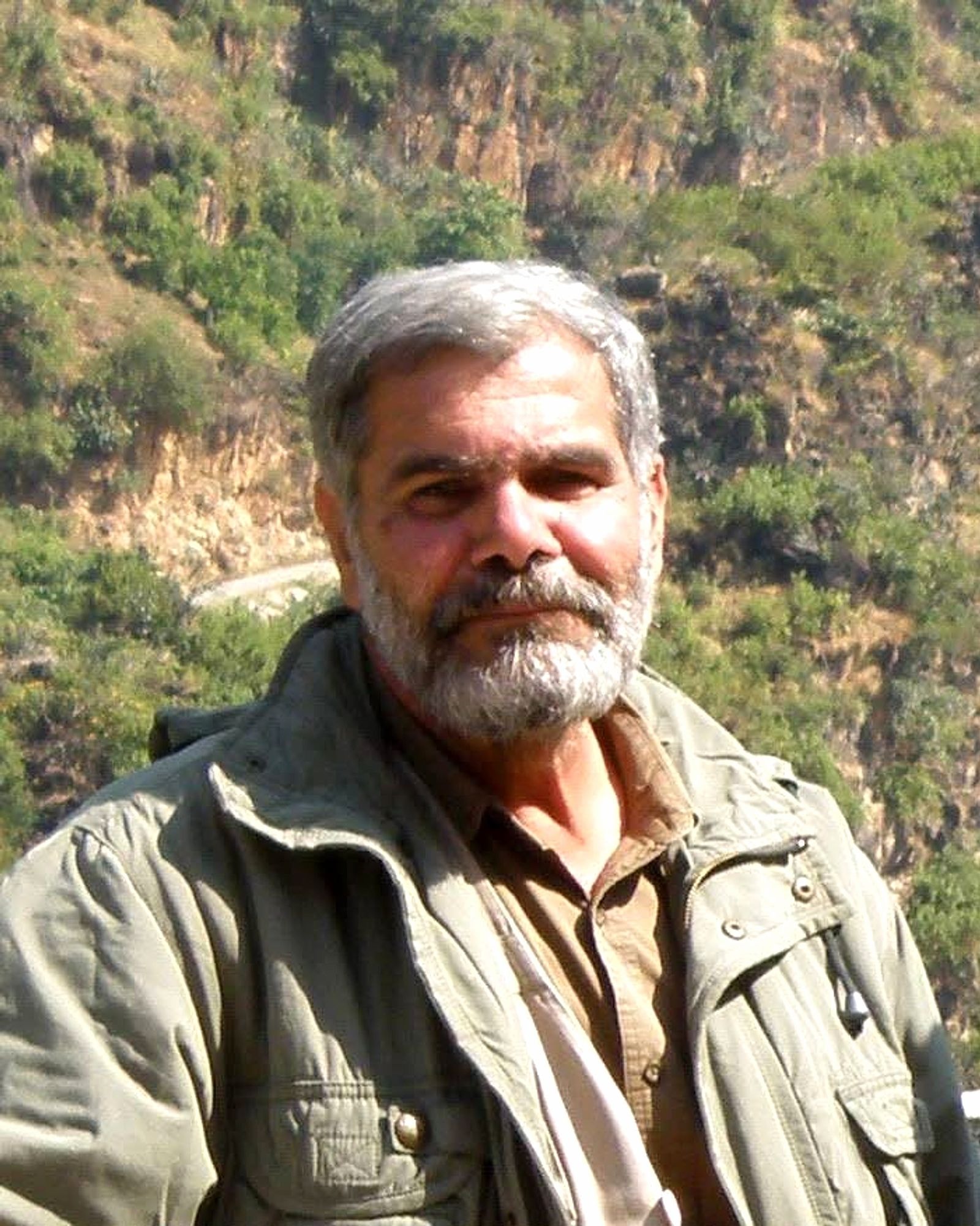 Shri Devendra Kumar Bhardwaj Ji, Lead Consultant for Ecology and Conservation, smiling in a green field jacket with forested hills behind him